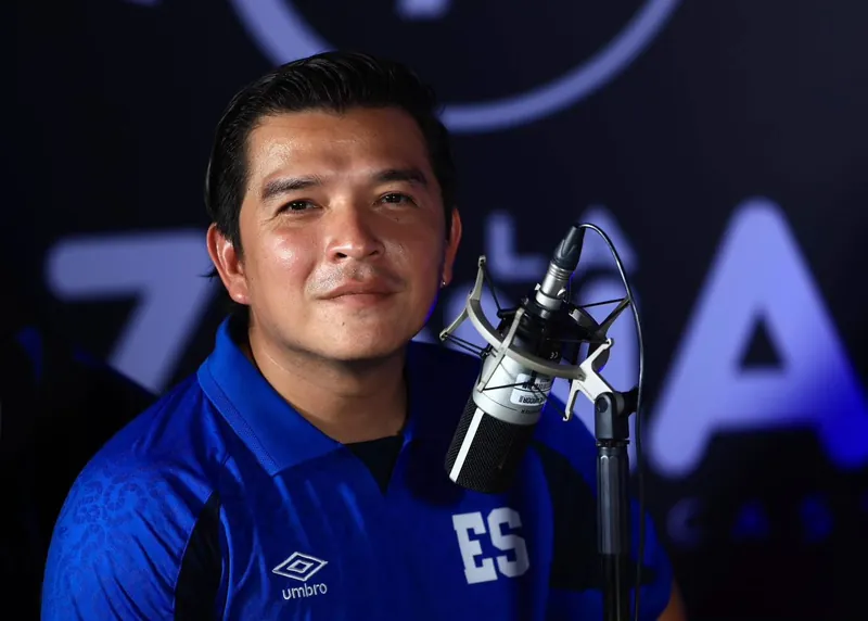 Moi Milian junto a un micrófono de estudio con la camiseta de El Salvador